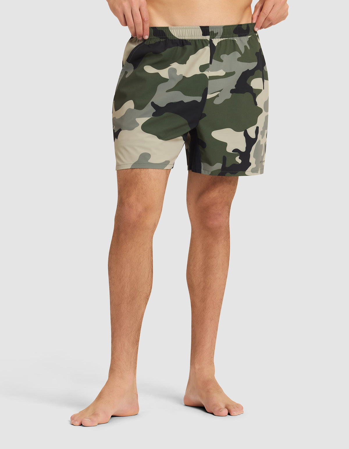 A person stands barefoot in Cozy Earth Men's Day & Night Shorts 5" against a plain light background, showing only the lower torso and legs. |Color:Cypress Camo