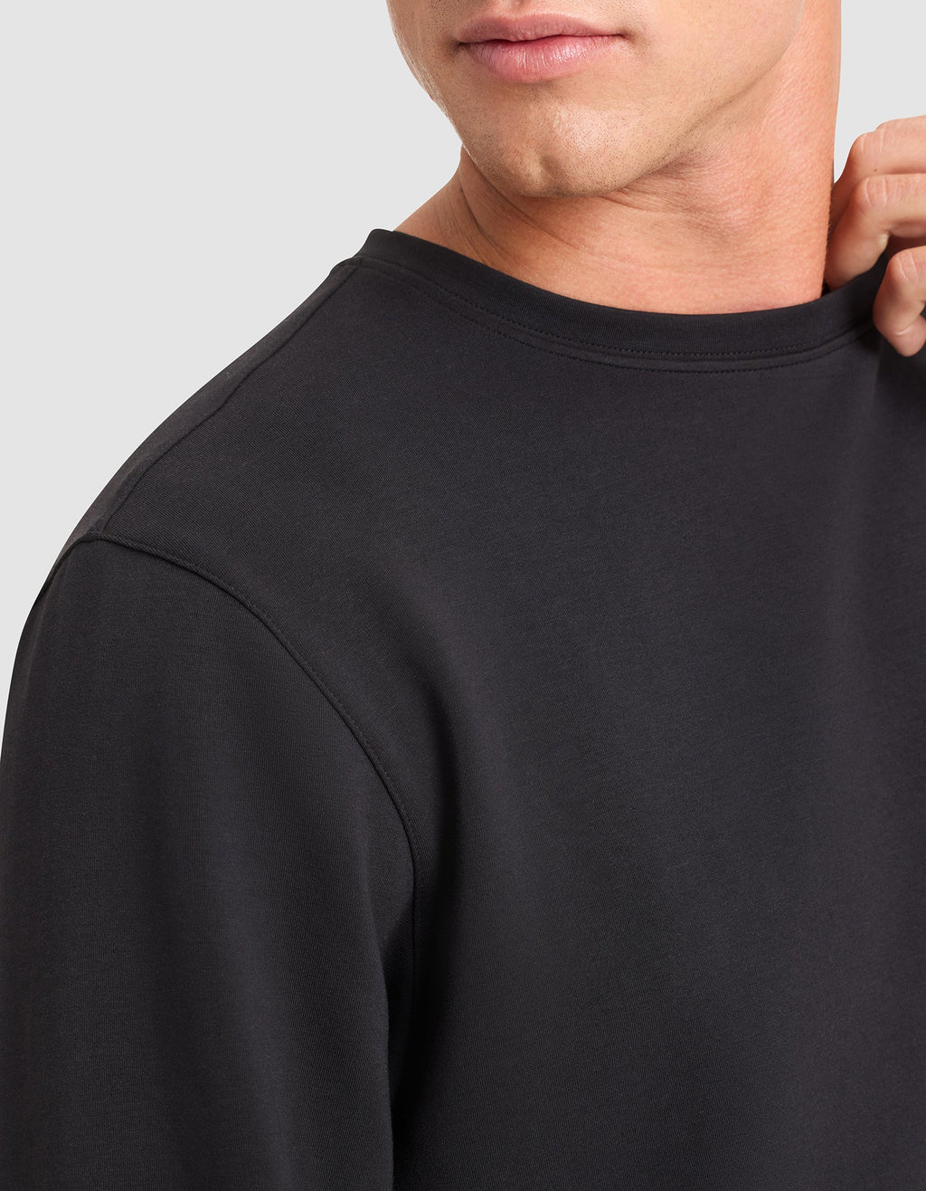 A close-up of a person wearing the Cozy Earth Men's StretchTech Crewneck in black, gently holding the collar. The image displays part of their face, neck, and upper torso. |Color:Jet Black
