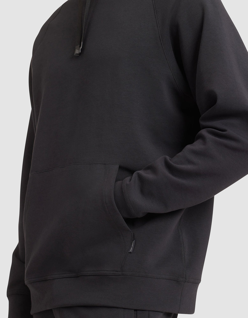 A man models the Cozy Earth Men's StretchTech Hoodie in black, one hand in the front pocket, shown from shoulders to hips against a plain light background. |Color:Jet Black