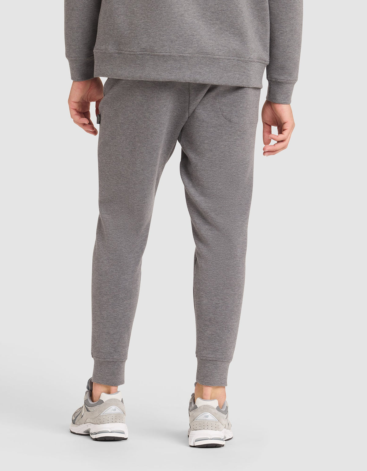 A person models the Cozy Earth Men's StretchTech Jogger in grey, paired with a matching sweatshirt and white sneakers, standing with their back to the camera against a plain white background. |Color:Coal Heather