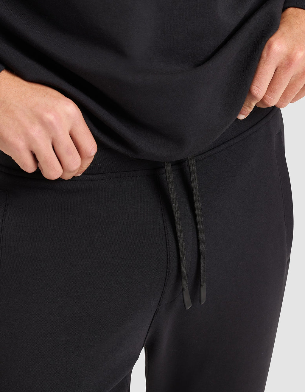 A person wearing Cozy Earth's Men's StretchTech Jogger, featuring a drawstring waist, stands with their hands near their waist. |Color:Jet Black