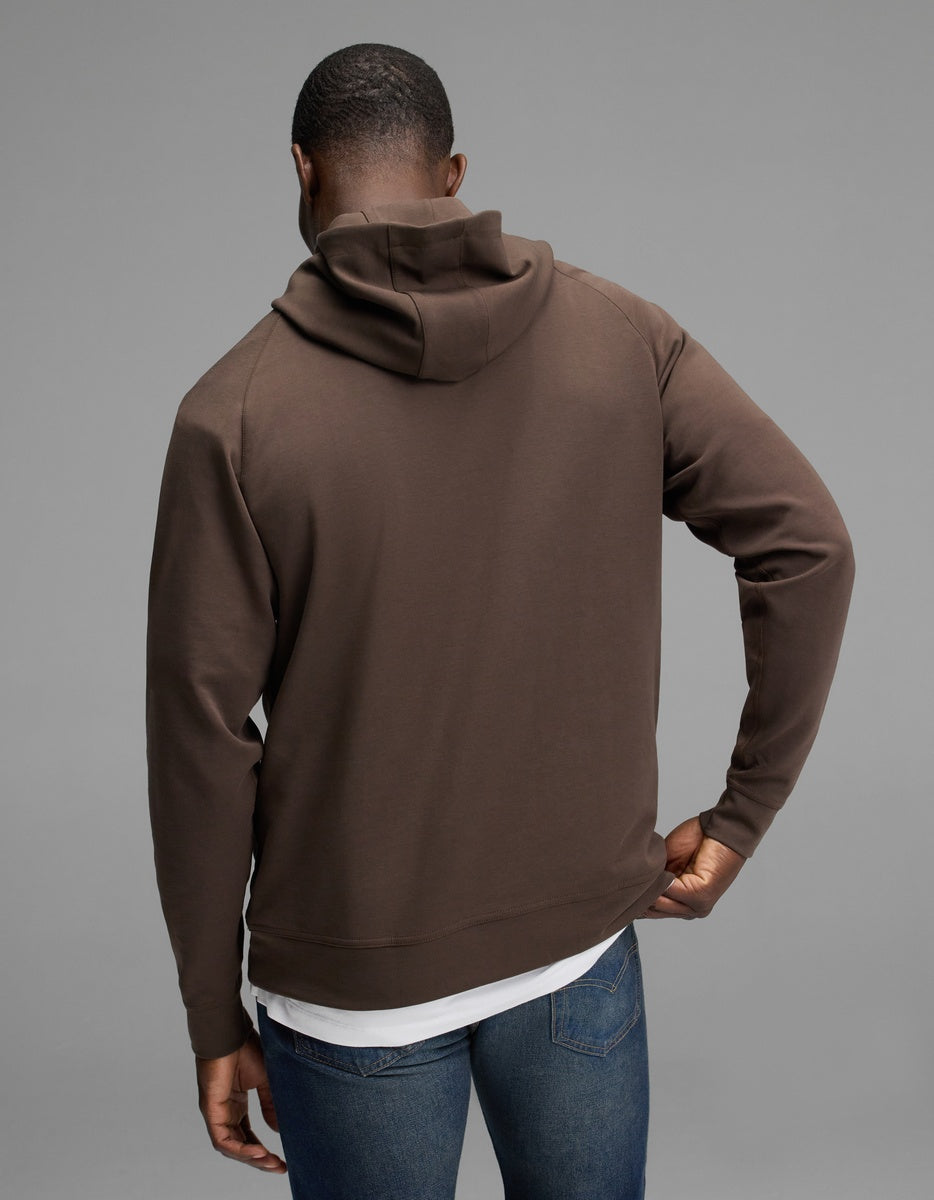 A person wearing the Cozy Earth Men’s StretchTech Hoodie in brown and blue jeans stands with their back to the camera against a plain gray background.|Color:Cacao