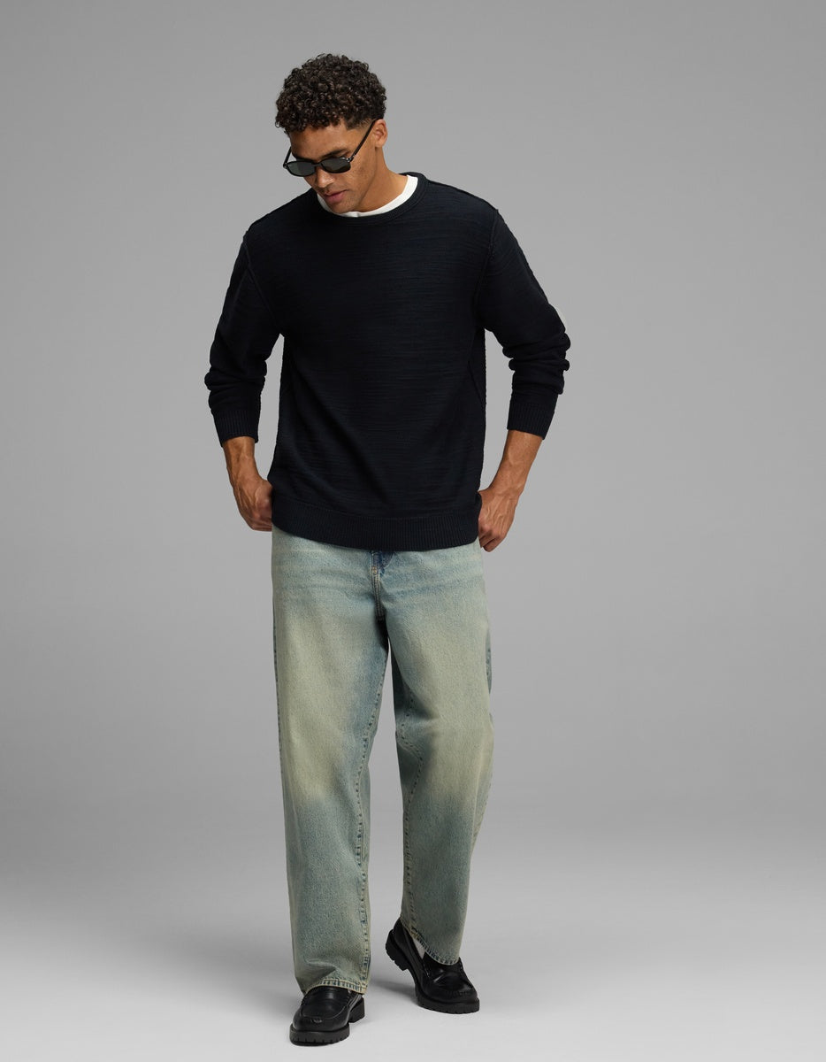 A person wearing a navy Cozy Earth Men’s Tate Crewneck, light-wash loose-fit jeans, and black loafers.|Color:Jet Black