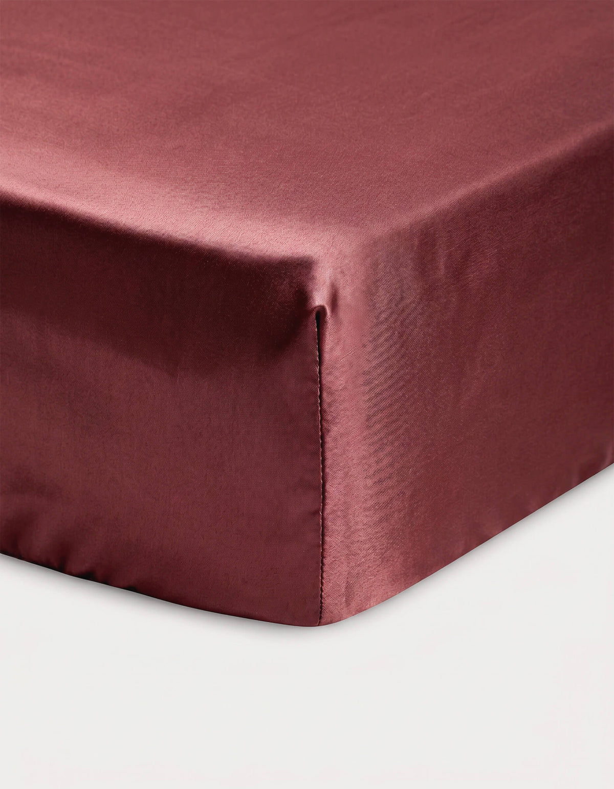 Close-up of a corner of a bed showcasing the Cozy Earth Bamboo Fitted Sheet in maroon, neatly covering the mattress against a white background.|Color:Mulberry