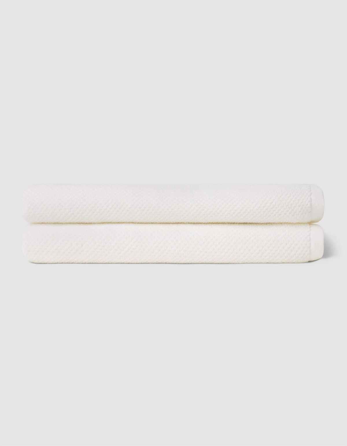 Two neatly folded Cozy Earth Nantucket Bath Sheets are stacked atop each other against a plain, light-colored background.|Color:White