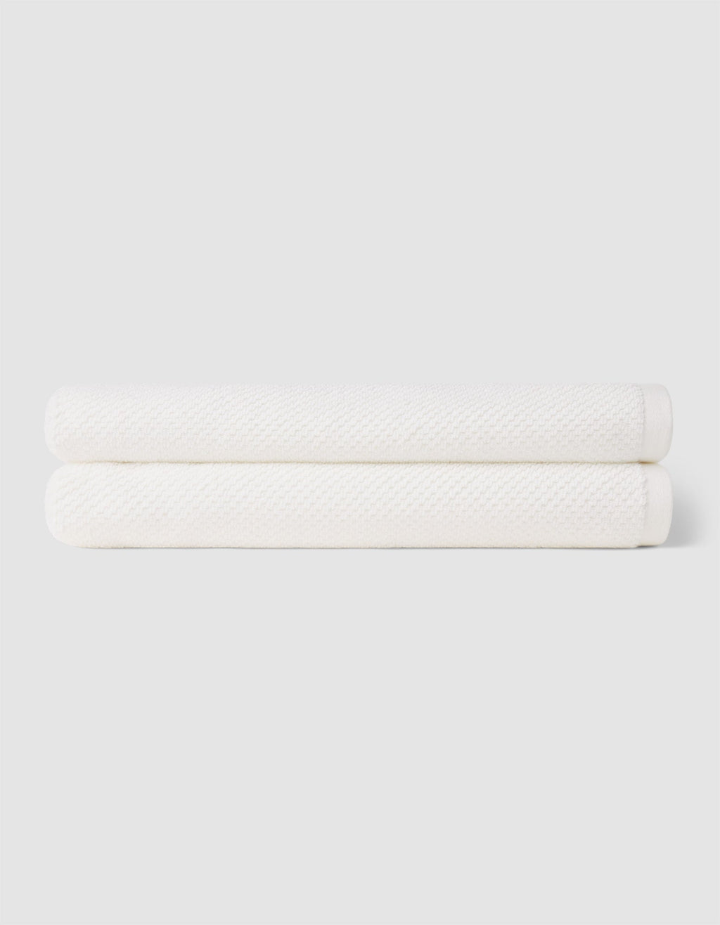 Two neatly folded Nantucket Bath Towels by Cozy Earth are stacked together against a plain light gray background.|Color:White