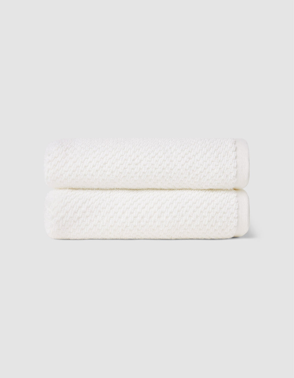 Two Nantucket Hand Towels by Cozy Earth, neatly folded and stacked, are displayed against a plain light gray background.|Color:White