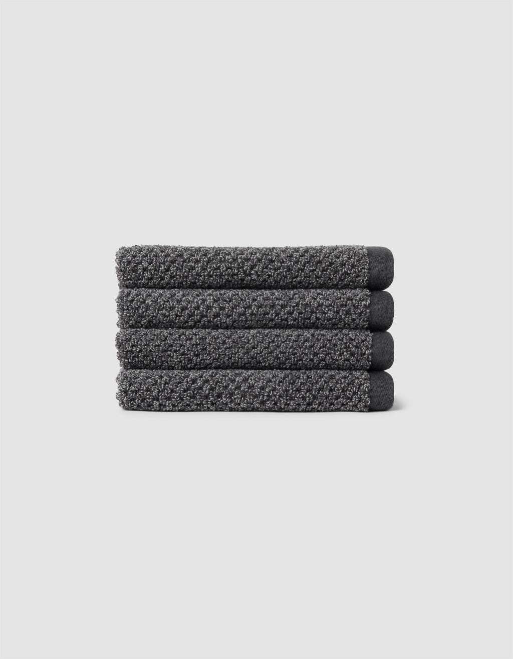 Four neatly folded Nantucket Washcloths by Cozy Earth, textured in dark gray, are stacked horizontally on a plain light gray background.|Color:Graphite