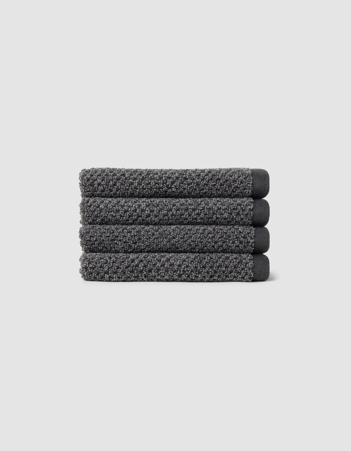 Four neatly folded Nantucket Washcloths by Cozy Earth, textured in dark gray, are stacked horizontally on a plain light gray background.|Color:Graphite