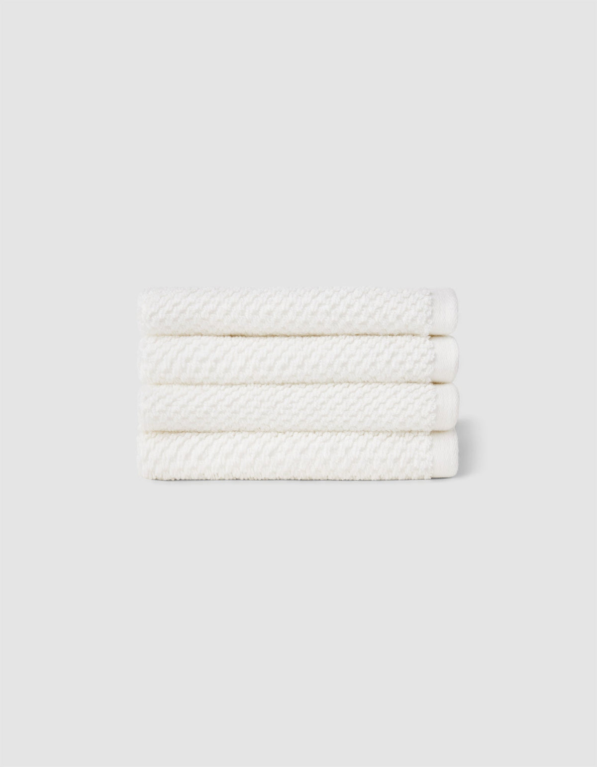 Four neatly folded Nantucket Washcloths by Cozy Earth, stacked horizontally against a plain light gray background.|Color:White