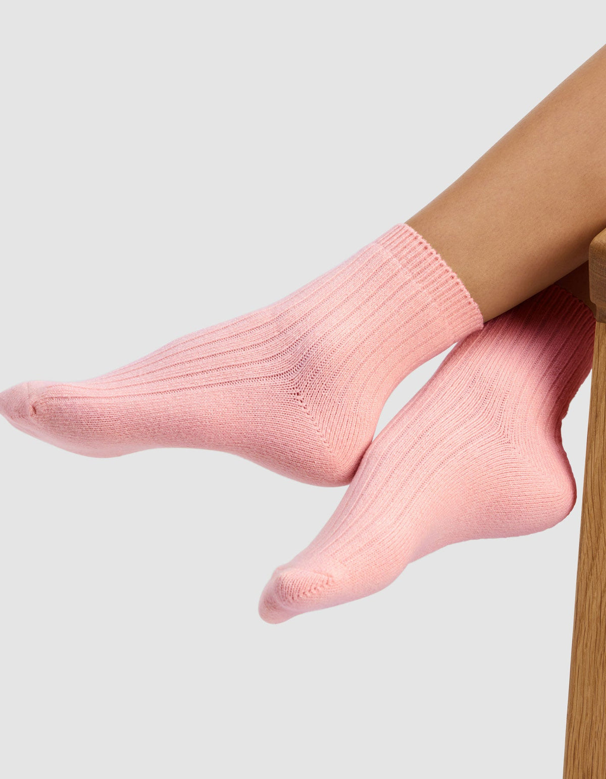 A person wearing The Plush Modern Crew Sock by Cozy Earth in light pink rests their feet on a wooden surface against a plain light gray background.|Color:Tulip