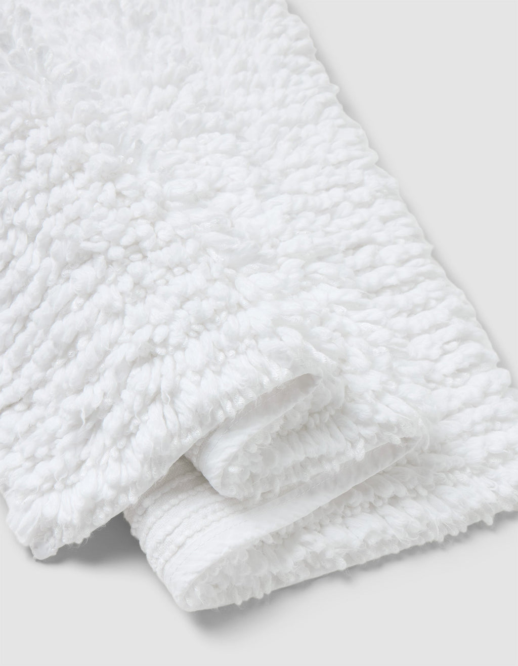 A close-up of the Cozy Earth Plush Loop Bath Mat, folded on a light gray background. The mat’s fluffy, looped texture highlights its softness and absorbency.|Color:White