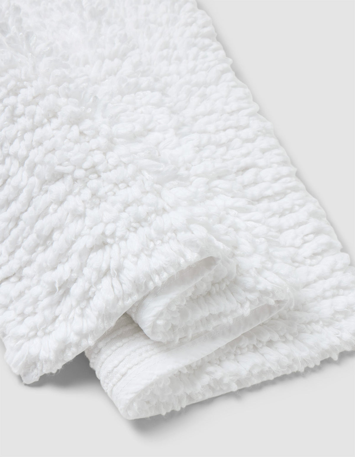 A close-up of the Cozy Earth Plush Loop Bath Mat, folded on a light gray background. The mat’s fluffy, looped texture highlights its softness and absorbency.|Color:White
