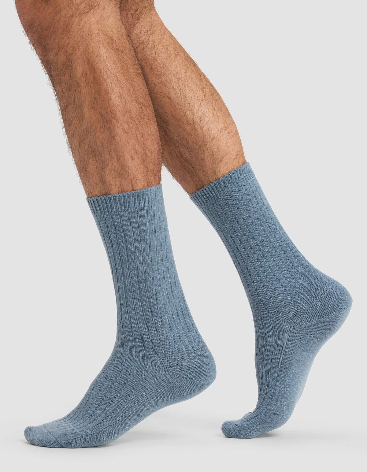 A person stands on tiptoe with one foot raised, showcasing Cozy Earth Men's Plush Lounge Calf Socks and their lower legs against a plain light background.|Color:Deep Blue