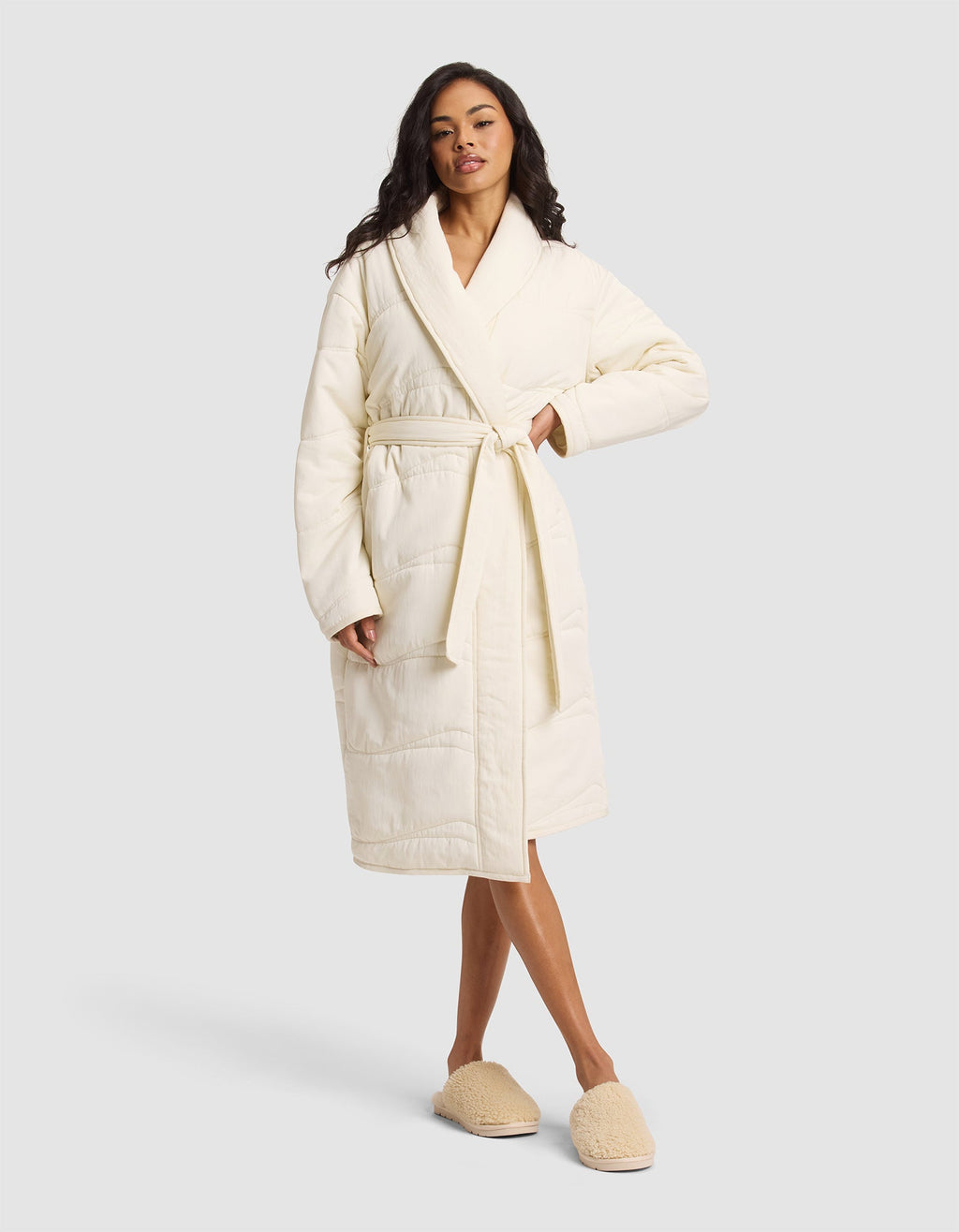 A woman wears the Cozy Earth Women's Quilted House Coat in Vanilla, featuring a waist tie and matching slippers, as she stands facing forward against a plain light gray background. |Color:Vanilla
