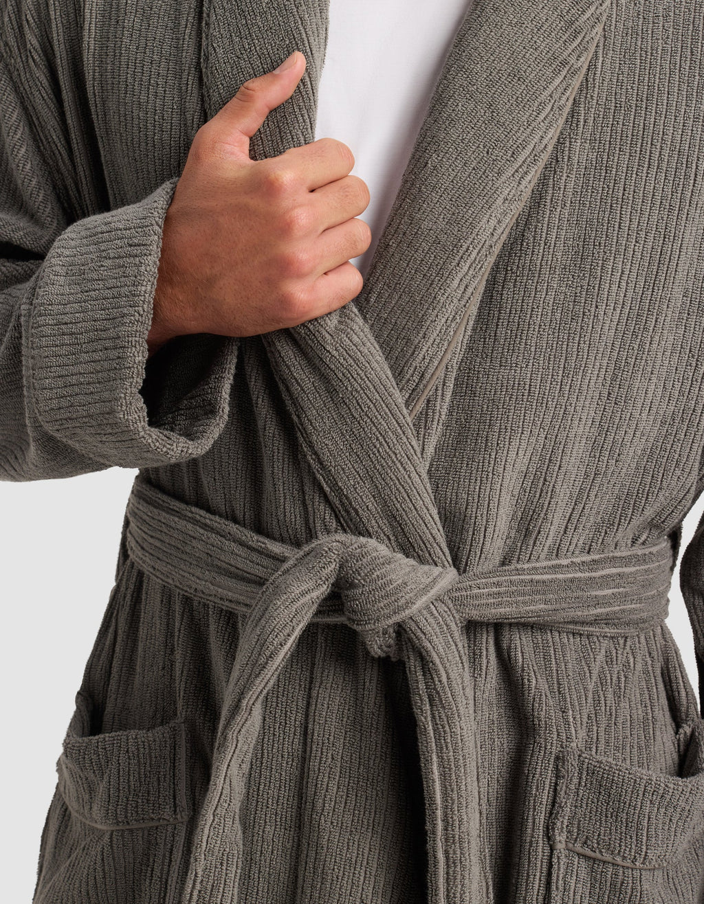 A person models Cozy Earth's Ribbed Terry Bath Robe in gray, tied at the waist, with one hand holding the lapel. The upper body, shirt underneath, and robe pockets are visible.|Color:Charcoal