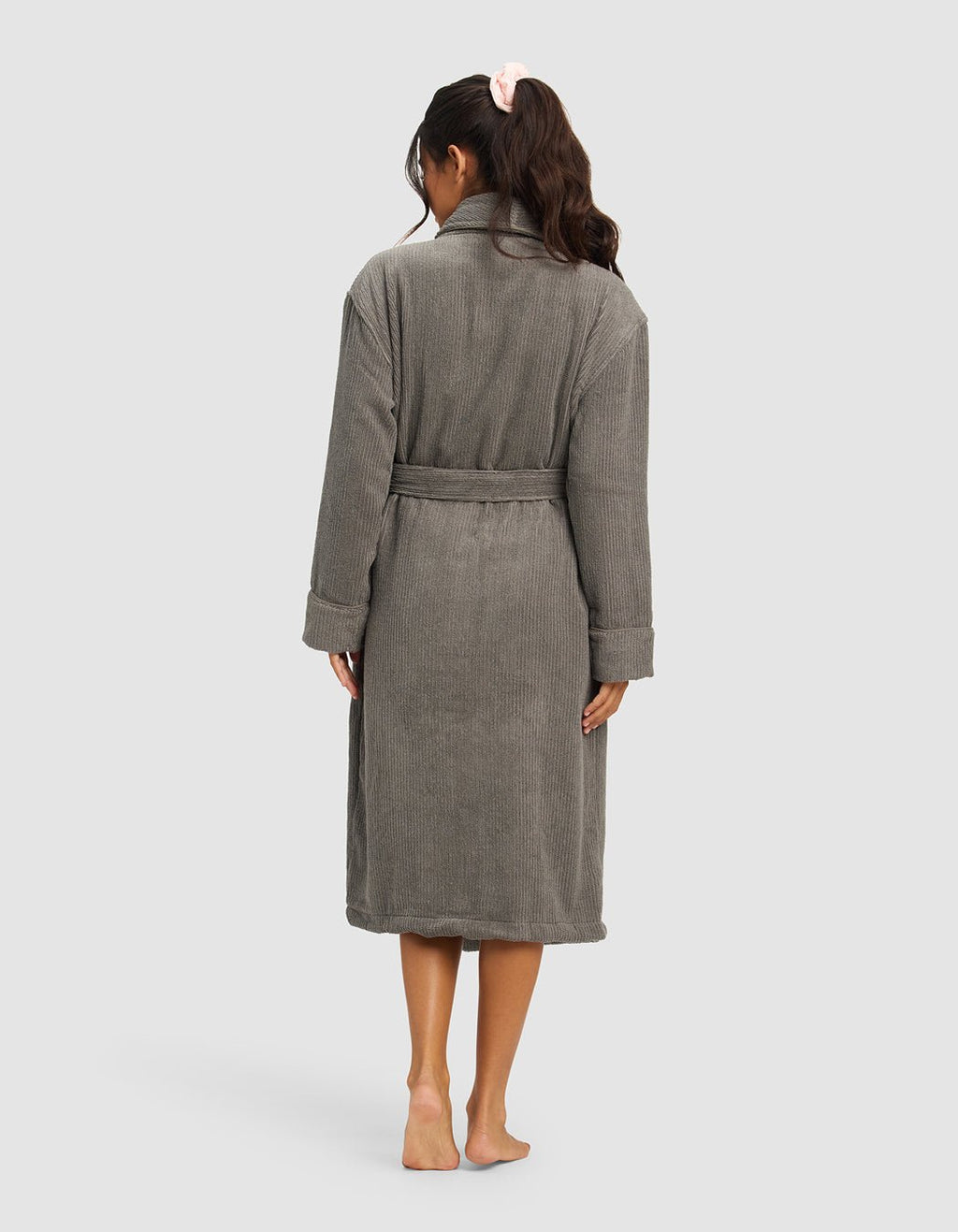 A woman stands barefoot facing away, wearing Cozy Earth's gray Ribbed Terry Bath Robe with a belt. Her long, wavy hair is tied back with a pink scrunchie against a plain light gray background.|Color:Charcoal