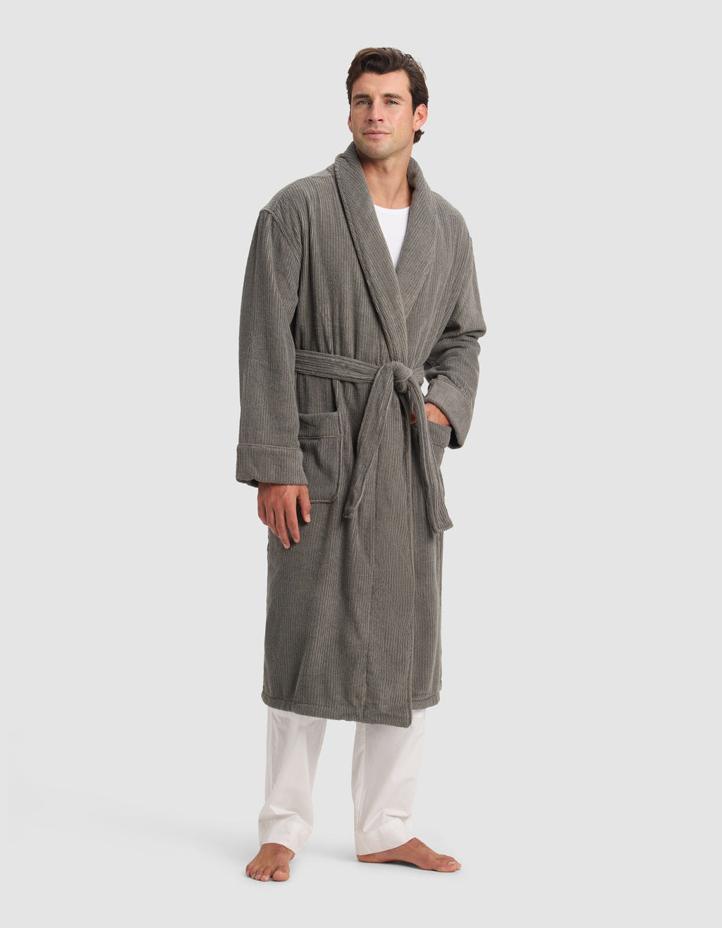 A man stands barefoot on a white background wearing the Cozy Earth Ribbed Terry Bath Robe in gray, with the belt tied at the waist. He has short brown hair and wears white pants and a white shirt underneath the robe.|Color:Charcoal