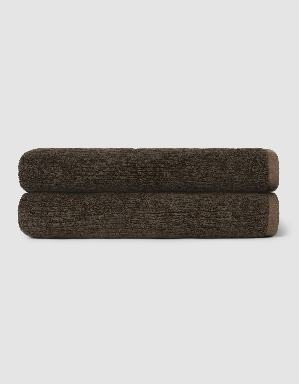 Two neatly rolled dark brown towels from the Cozy Earth Complete Ribbed Terry Bath Bundle are stacked on top of each other against a plain, light background.|Color:Espresso