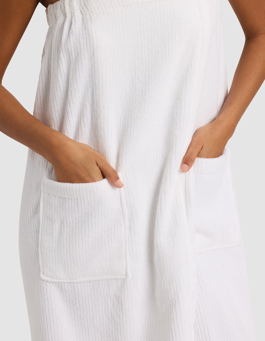 A person wears the Cozy Earth Ribbed Terry Bath Wrap, hands tucked into its large front pockets. Only their torso and hands are visible against a plain light background.|Color:White