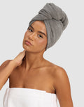 A woman poses against a plain light background, wearing the Cozy Earth Ribbed Terry Hair Towel on her head and a white towel around her body, with one hand gently touching her neck.|Color:Charcoal