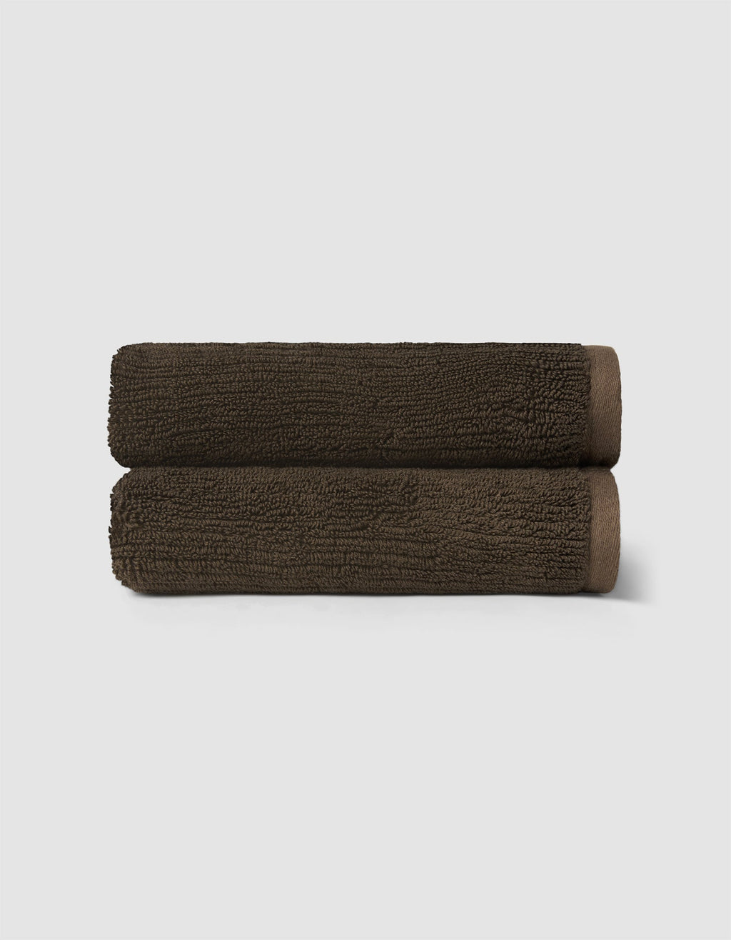 Two neatly rolled, dark brown towels from the Cozy Earth Complete Ribbed Terry Bath Bundle are stacked against a plain light gray background.|Color:Espresso