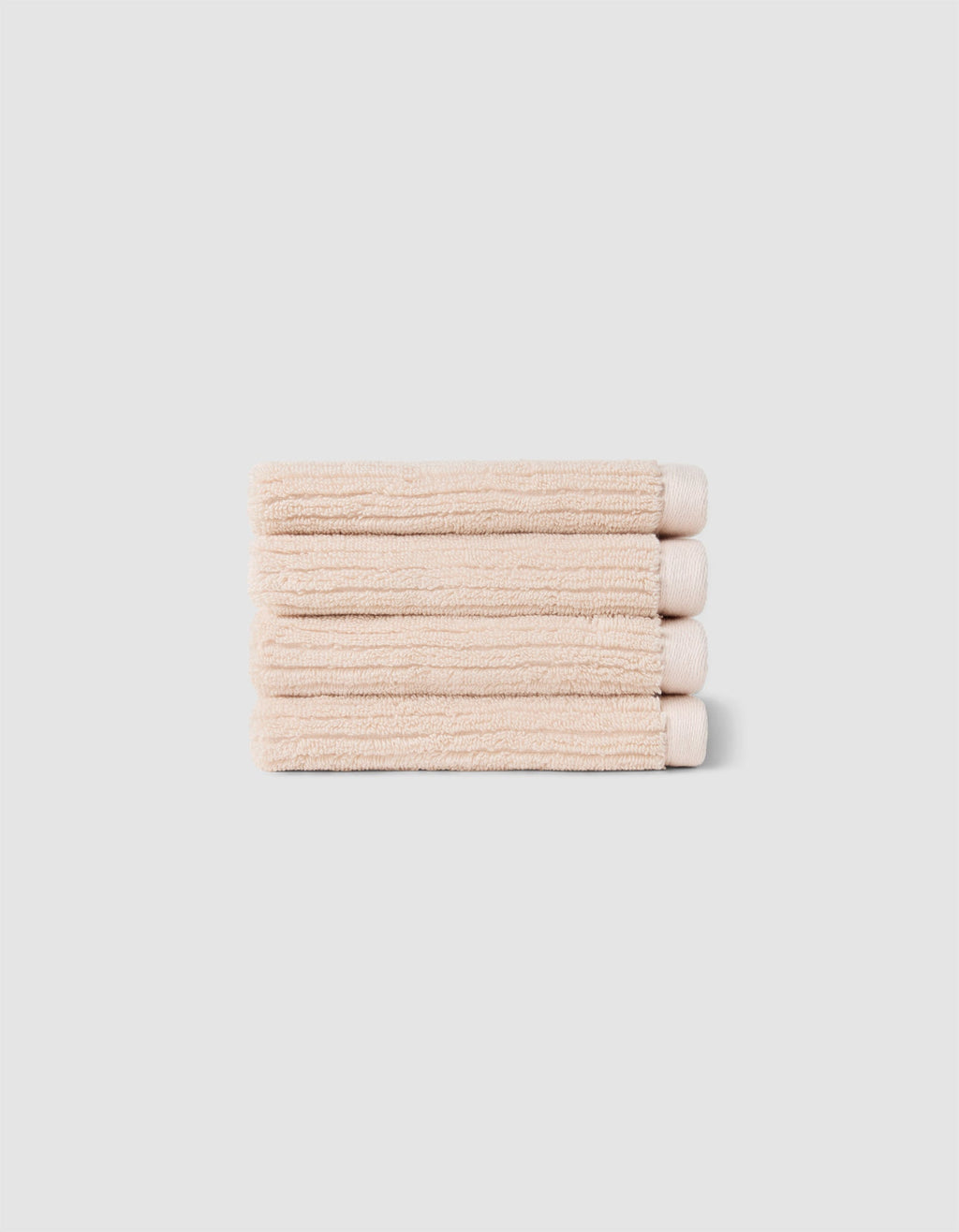 The Complete Ribbed Terry Bath Bundle by Cozy Earth features four neatly folded beige towels stacked atop each other against a plain light gray background.|Color:Petal