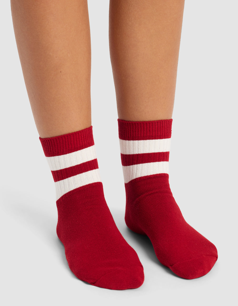A person wearing Cozy Earth Women's Sadie Socks—red with two white horizontal stripes near the top—stands on a light gray surface.|Color:Crimson/Bone