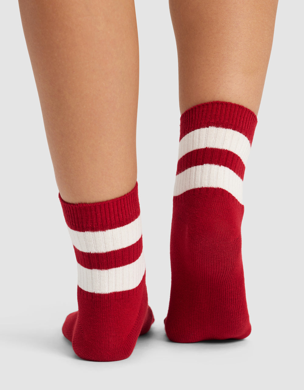 A close-up of two legs wearing Cozy Earth Women's Sadie Socks in red, featuring two white stripes near the top, shown against a plain light gray background.|Color:Crimson/Bone