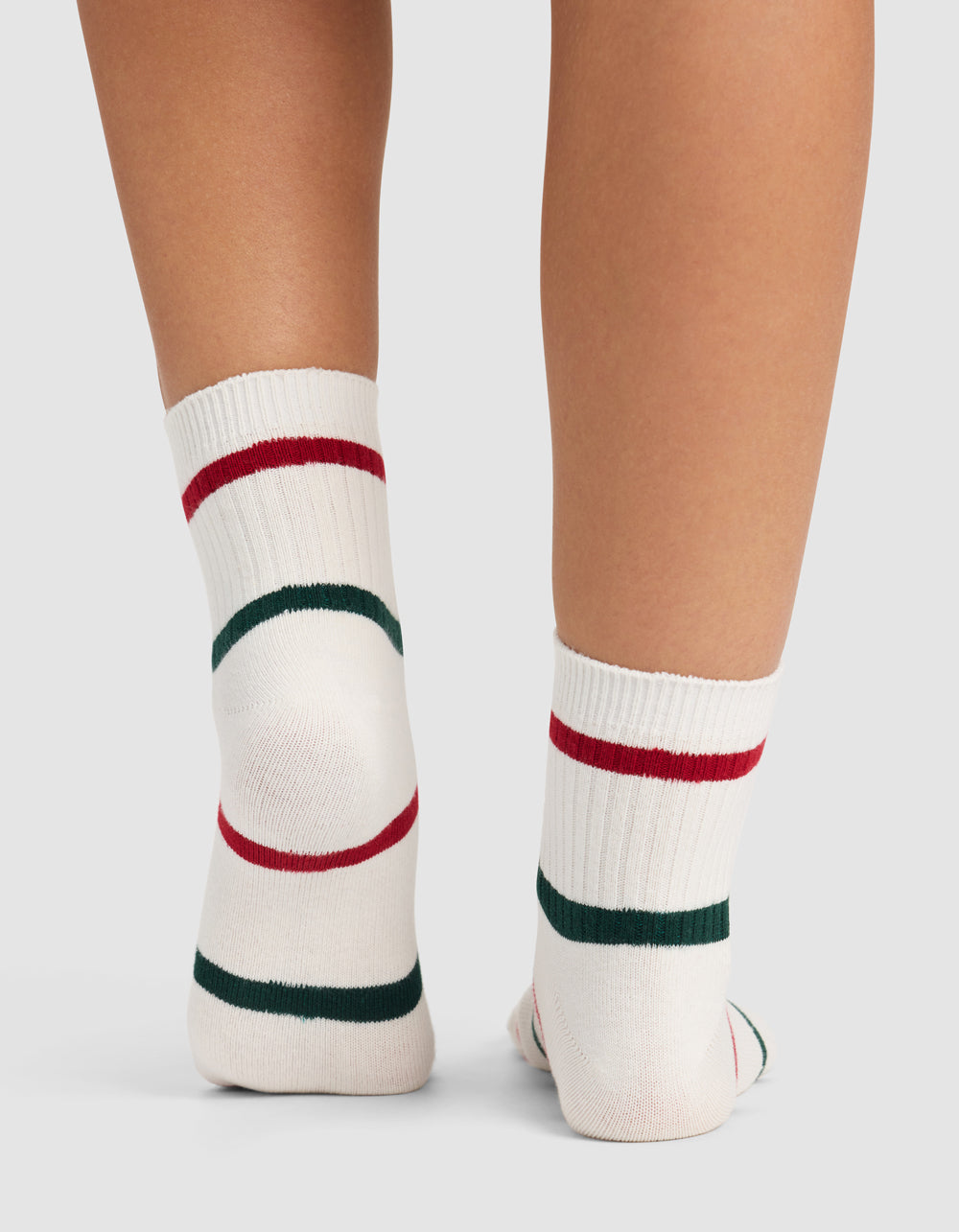 A close-up of two legs wearing Cozy Earth Women's Sadie Socks—white with red and green stripes—standing on a light surface. |Color:Jade/Crimson