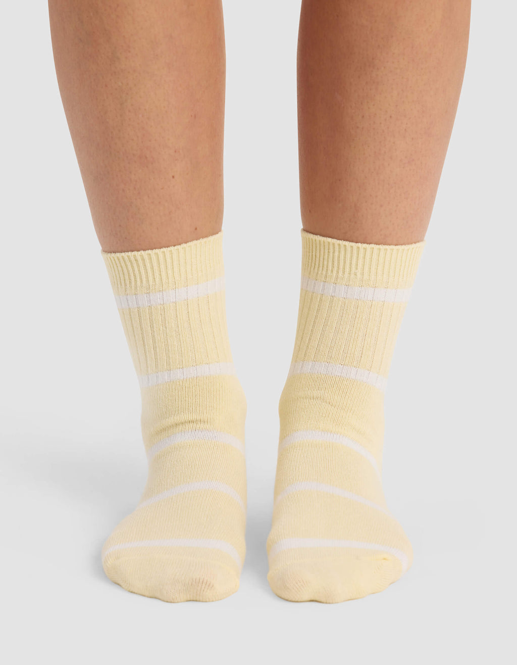 A person wearing Cozy Earth Women's Sadie Socks in yellow with white horizontal stripes stands on a light-colored surface; only their lower legs and feet are visible.|Color:Sea Salt/Meringue