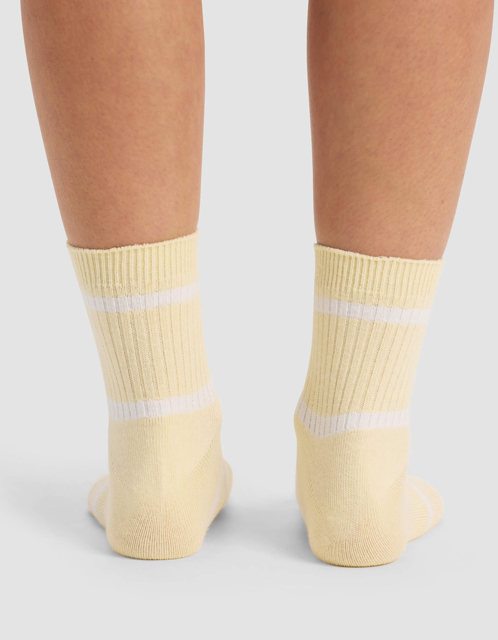 A close-up of two feet wearing Cozy Earth Women's Sadie Socks in yellow with white stripes, standing on a light-colored surface.|Color:Sea Salt/Meringue