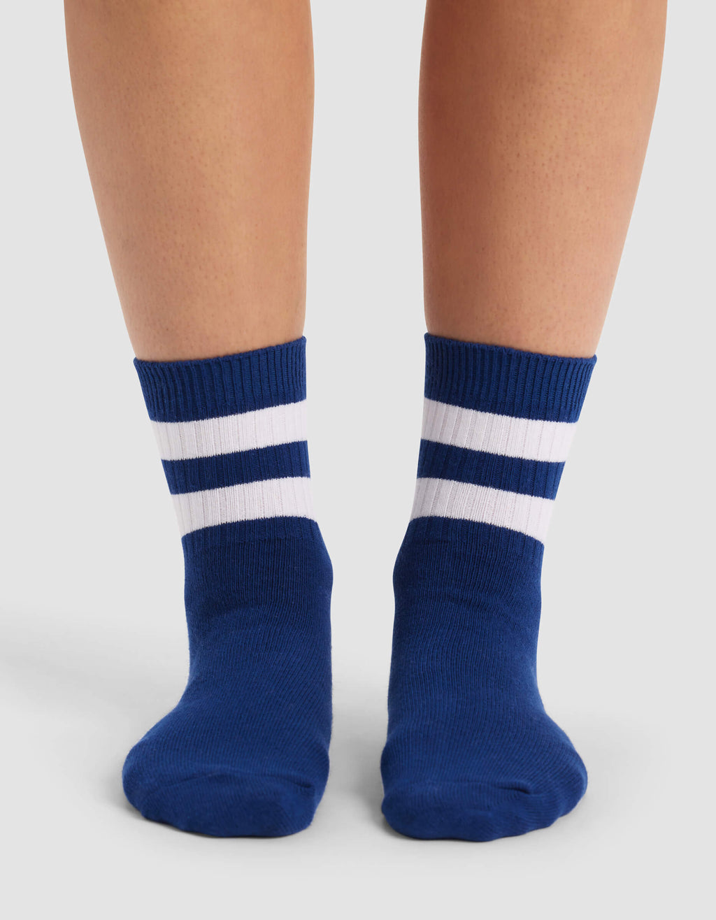 A person wears Cozy Earth's Women's Sadie Sock—blue with two white horizontal stripes near the top—while standing on a light surface.|Color:Pacific/White