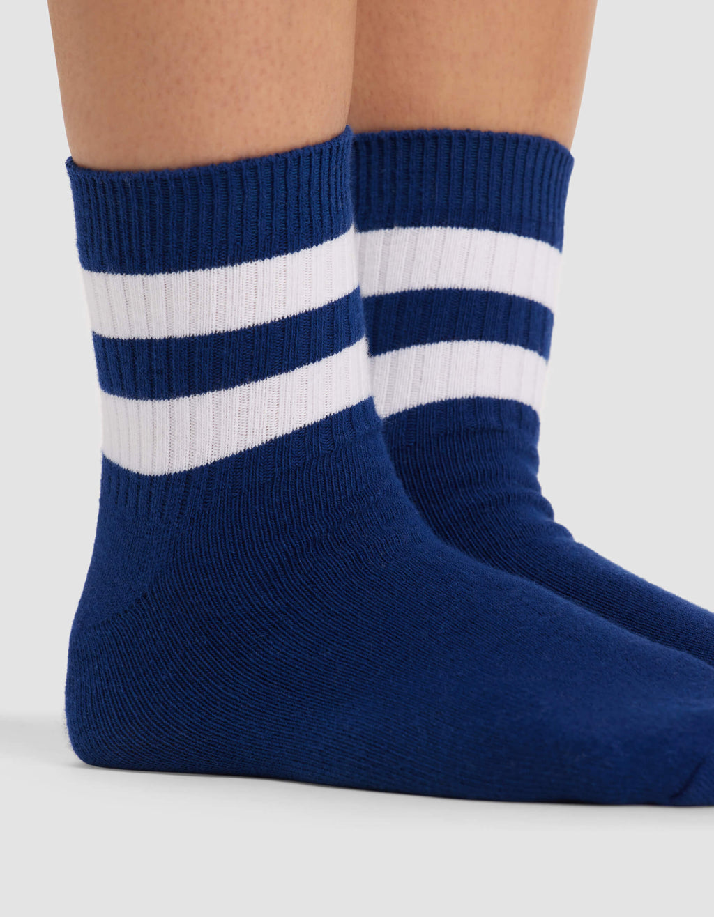 Close-up of two feet wearing Cozy Earth Women's Sadie Sock in blue with two white stripes near the top, standing on a light surface.|Color:Pacific/White