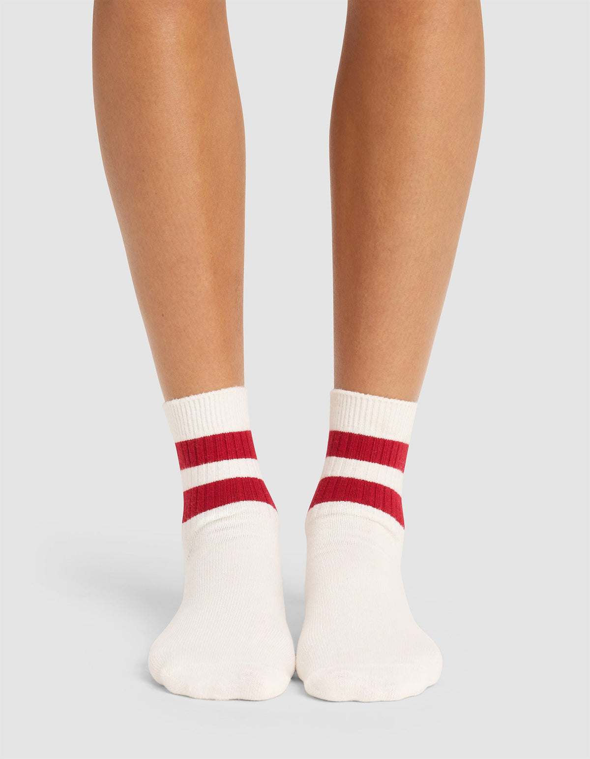A person wears Cozy Earth's Women's Sadie Sock—white with red and white ankle stripes—standing barefoot and photographed from behind against a plain light background. |Color:Bone/Crimson
