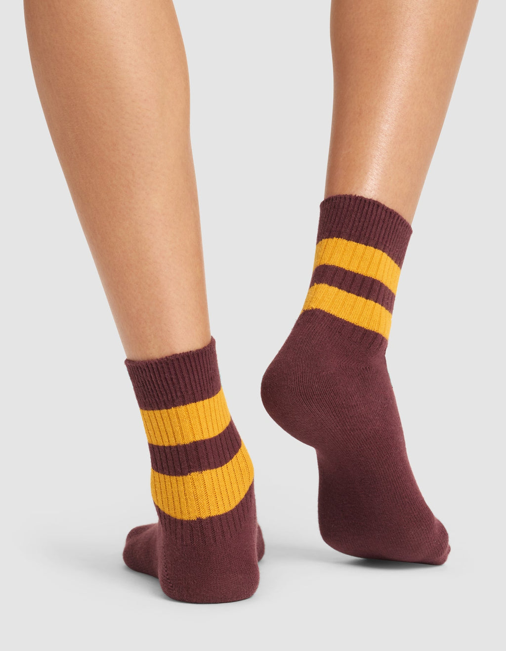A person wearing Cozy Earth's Women's Sadie Sock—maroon with two thick yellow stripes near the top—stands on a white background, showing only their lower legs and feet. |Color:Burgundy/Goldenrod