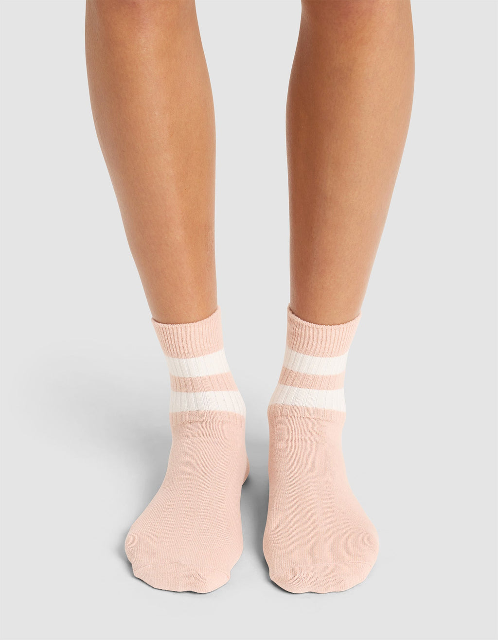 A person stands on a light surface wearing Cozy Earth Women's Sadie Socks in pale pink with two white stripes near the cuffs; only their lower legs and feet are visible. |Color:Dusty Rose/Bone