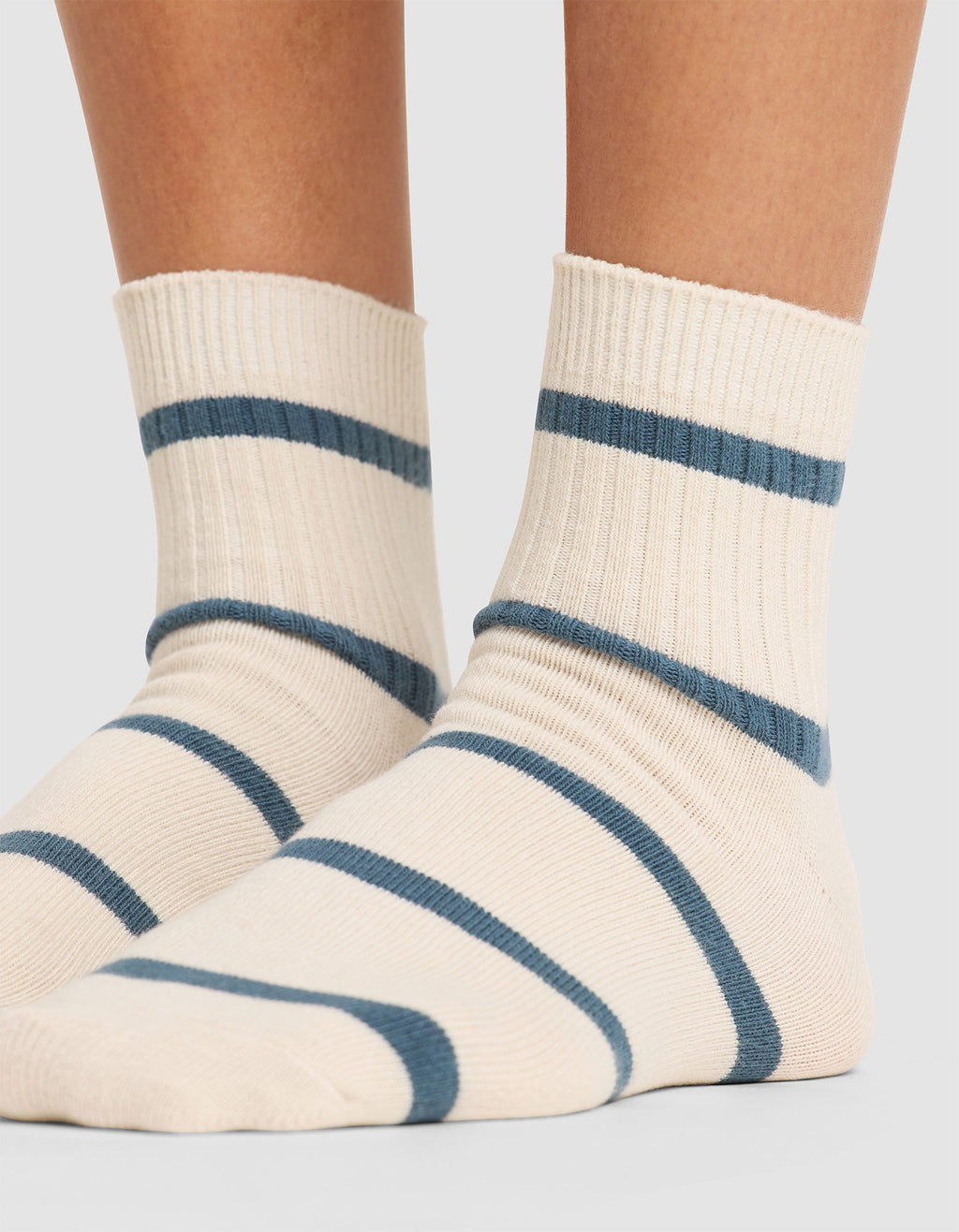 Close-up of a person wearing Cozy Earth's Women's Sadie Sock in cream with blue stripes, standing on a light gray surface. Only the lower legs and feet are shown. |Color:Mineral/Oceanside
