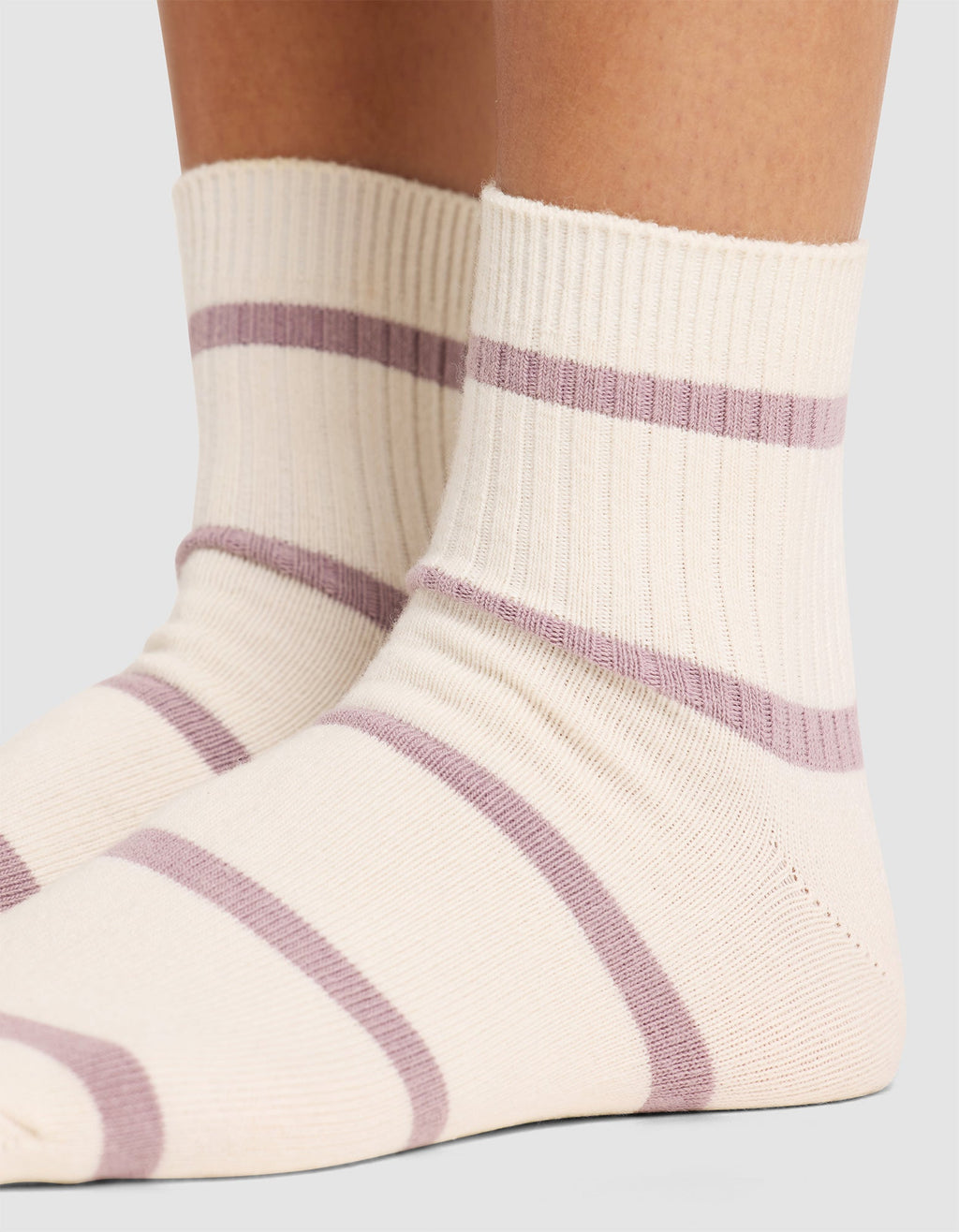 Close-up of two feet wearing Cozy Earth Women's Sadie Socks, featuring cream color with ribbed cuffs and horizontal light purple stripes, standing on a neutral surface. |Color:Parchment/Dusty Orchid