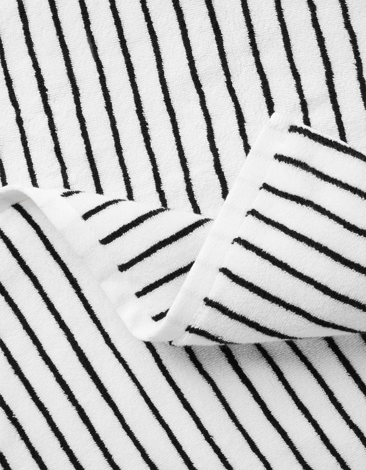 A close-up of Cozy Earth’s Complete Striped Luxe Bath Bundle shows white fabric with thin black vertical stripes; a folded corner reveals the matching striped pattern on both sides. |Color:Black Stripe