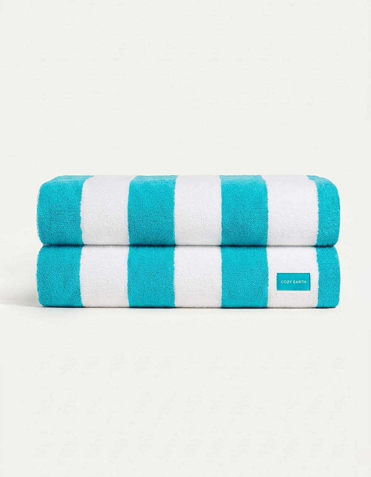 The Seaside Resort Towel Bundle by Cozy Earth features two neatly folded towels with bold turquoise and white stripes, stacked on a plain light background. A small Cozy Earth fabric label is visible on the lower towel.|Color:Aqua Stripe