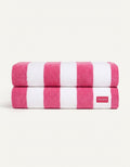 Two neatly folded towels from the Seaside Resort Towel Bundle by Cozy Earth, featuring wide pink and white stripes, are stacked together. A small white tag with red "COZY EARTH" text is visible on the bottom towel.|Color:Punch Stripe