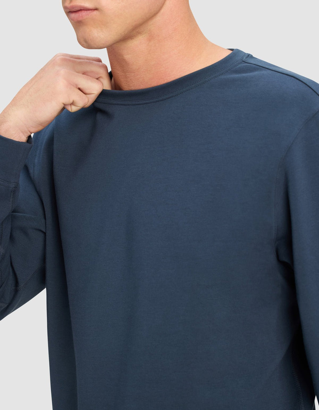 A person wearing the Cozy Earth Men's StretchTech Crewneck in dark blue, holding the neckline with one hand, shown from shoulders to chin against a light grey background.