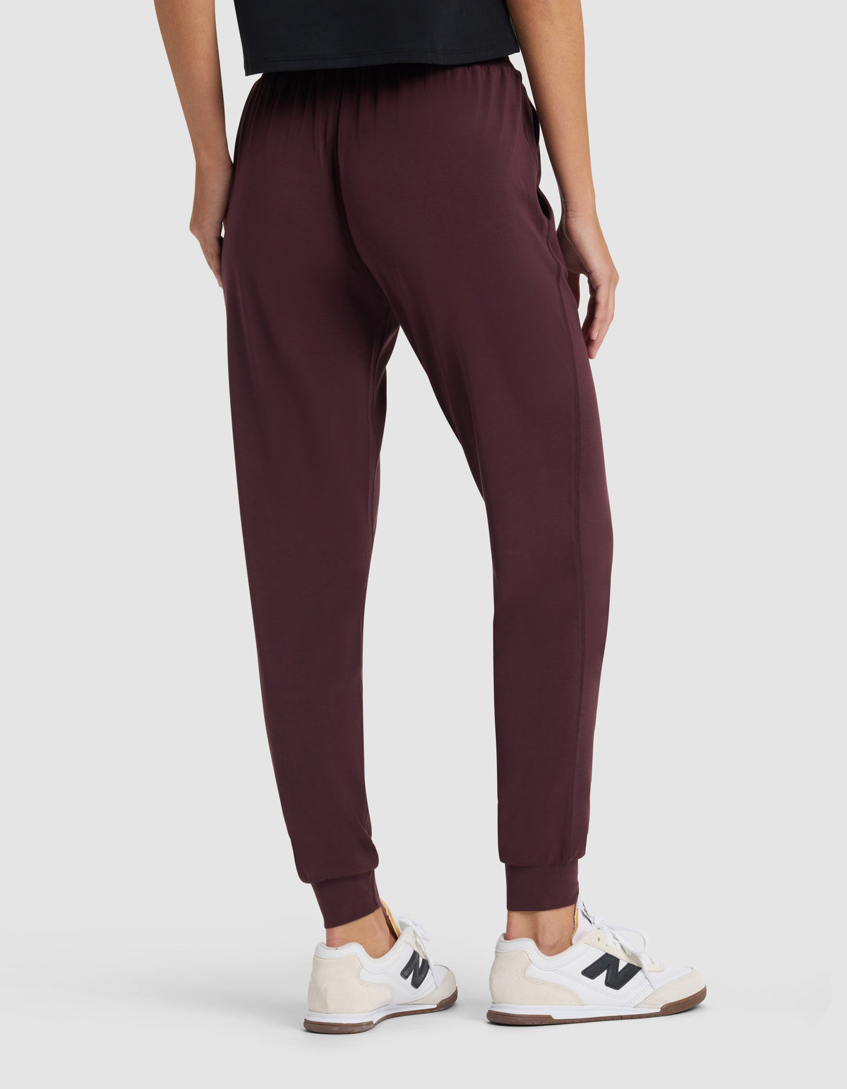 A person wearing Cozy Earth Women's Studio Jogger in burgundy and white sneakers, shown from the back with only their lower half visible against a plain light background.|Color:Raisin