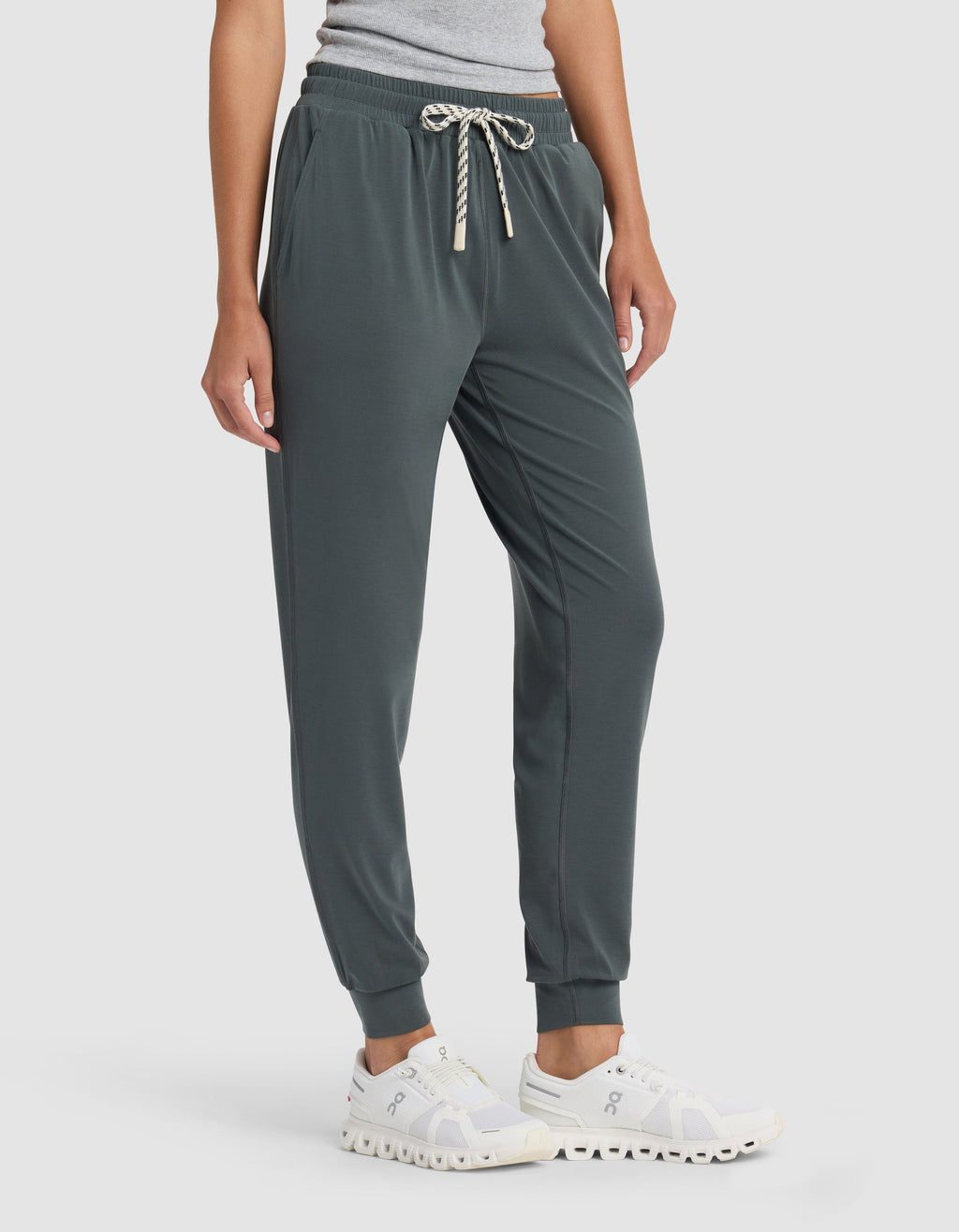 A person wearing Cozy Earth's Women's Studio Jogger in dark green, paired with a light gray top and white athletic shoes, stands against a plain light background.|Color:Storm