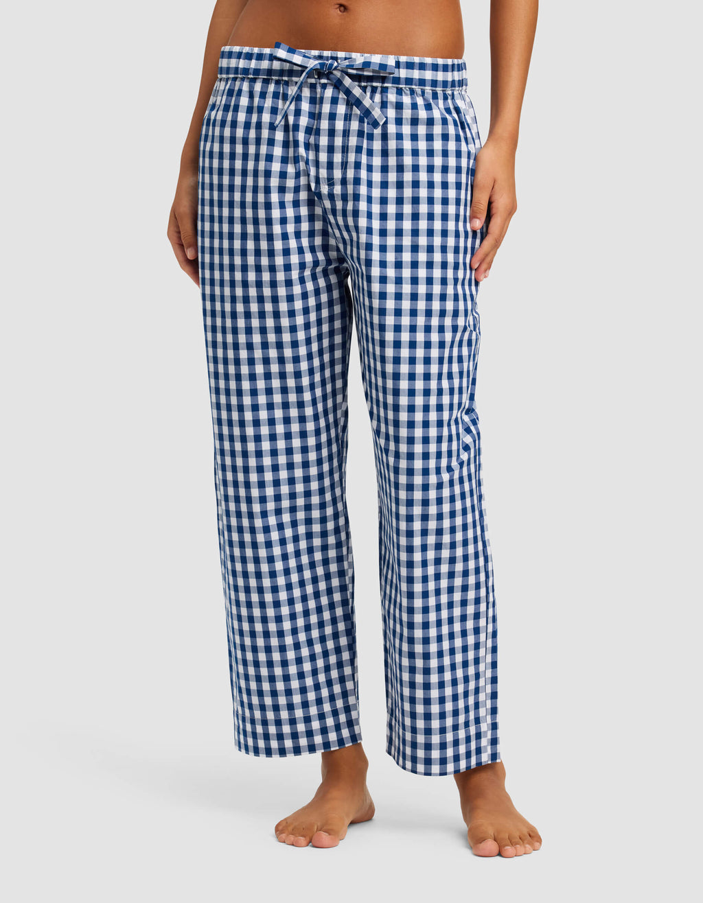 A person models Cozy Earth's Women's Sutton Short Sleeve & Pant Pajama Set—blue and white checkered pants with an elastic waistband and drawstring—standing barefoot against a plain background. The upper body is not shown.|Color:Pacific Gingham
