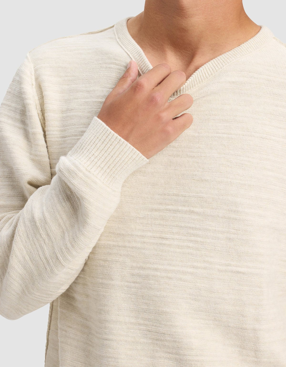 A man models the Cozy Earth Men's Tate Crewneck, a cream-colored knit sweater with long sleeves, shown from shoulders to waist against a plain light gray background. One hand touches the collar near his neck.|Color:Alabaster