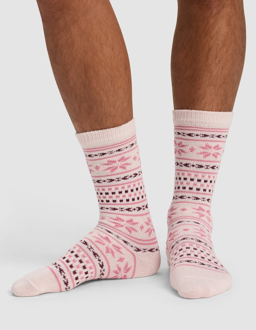 A person wearing Cozy Earth's The Snowflake Plush Lounge Sock in light pink with dark pink and black geometric and floral patterns stands on a white background.|Color:Ballet