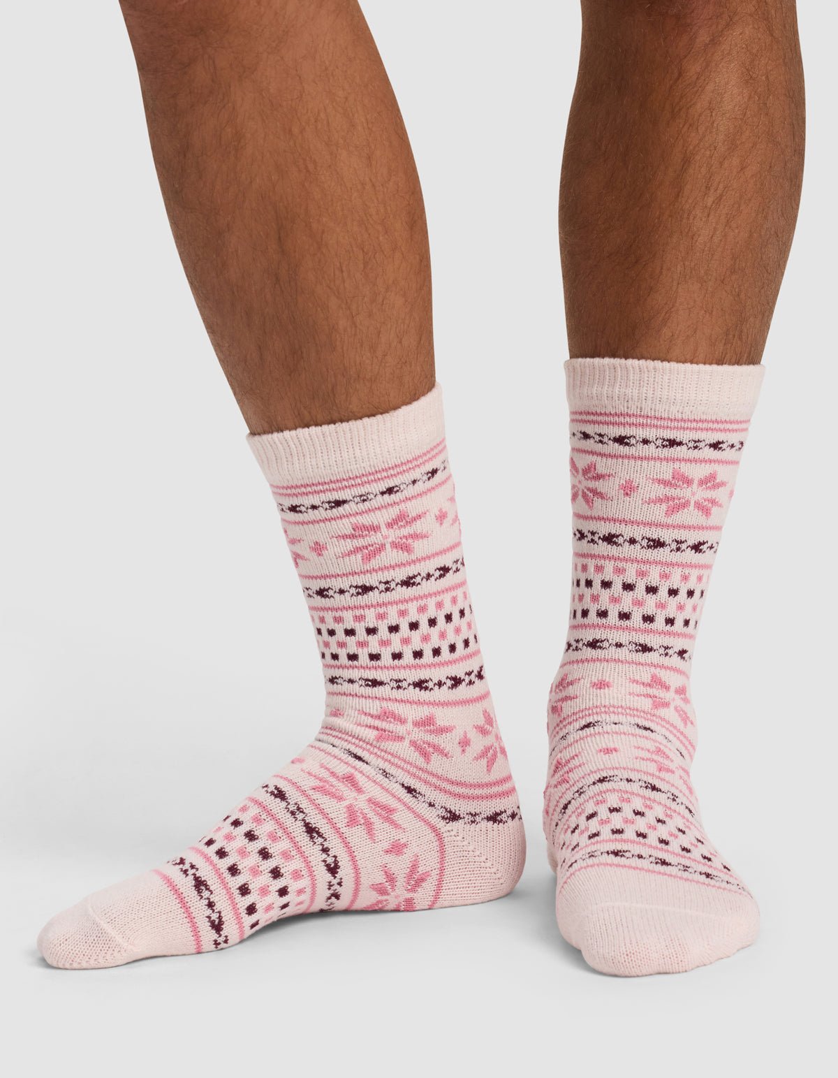 A person wearing Cozy Earth's The Snowflake Plush Lounge Sock in light pink with dark pink and black geometric and floral patterns stands on a white background.|Color:Ballet