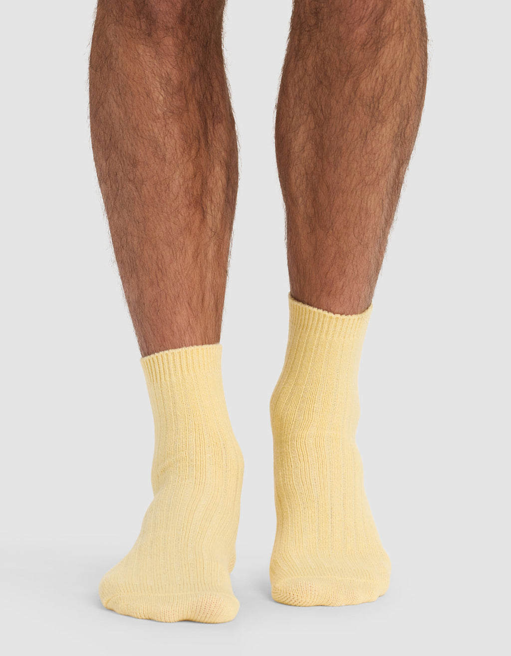 A person stands on a light surface, shown from the calves down, wearing Cozy Earth's Plush Lounge Quarter Socks in pale yellow. Their feet are close together, set against a neutral gray background.|Color:Daisy